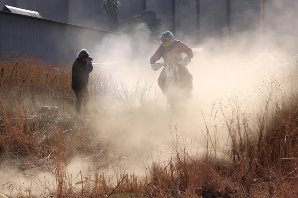 Motorbike airborne over bump in dust on sand track during rally — ストック写真