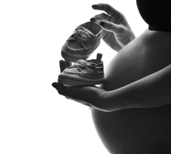Живіт молодої вагітної жінки, що стоїть з маленьким дитячим черевиком — стокове фото