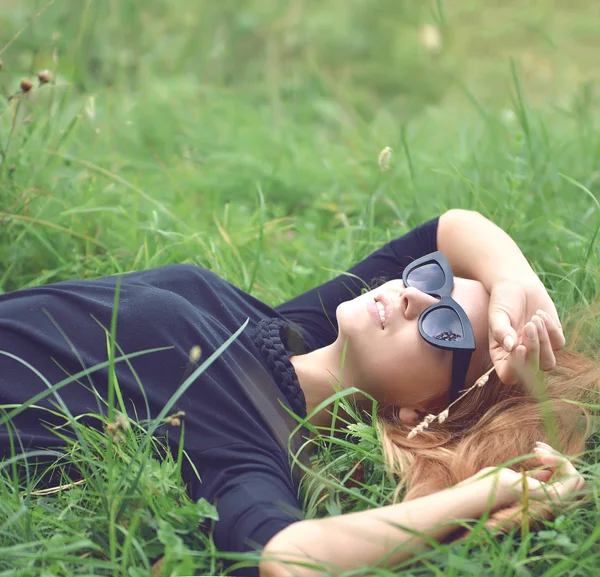 Vrouw houden handen achter het hoofd en het glimlachen in zonnebril liegen — Stockfoto