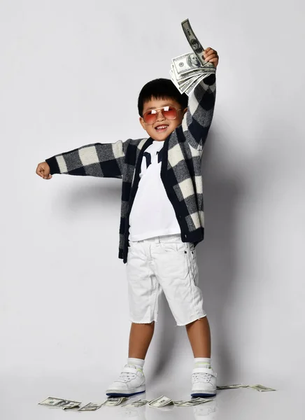 Šťastný usměvavý asijský bohatý kluk milionář v moderních slunečních brýlích zvedl ruku s dolary nahoru cash bunch of money Lucky winner — Stock fotografie