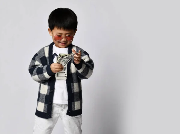 Glimlachende Aziatische rijke jongen miljonair in een moderne zonnebril telt dollars contant geld dat hij in de hand heeft. Gelukkige winnaar — Stockfoto