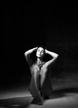 Siyah ve beyaz. Mücevherli şehvetli çıplak kadın elleri başının üstünde yerde oturuyor, parmaklarını saçlarında gezdiriyor.