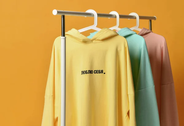 Yellow blue and pink hoodies with embroidered text on hangers in the wardrobe clothes shop. Translation: Love Myself — Stock Photo, Image