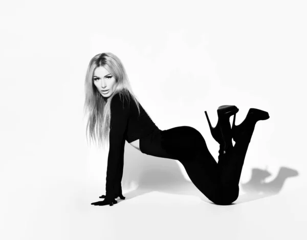 Slanke blonde vrouw met pruillip in strak zwart overall pak en hoge hakken schoenen staat op handen en voeten sexy poseren — Stockfoto