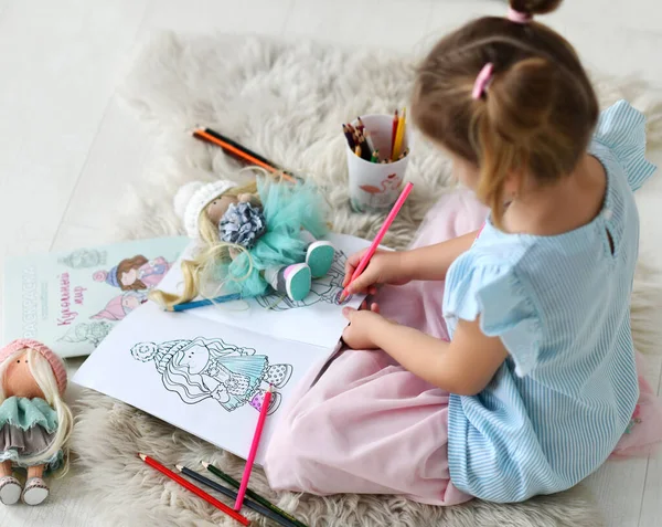 Menina pequena em casa roupas sentadas no tapete macio e desenho boneca para colorir com lápis coloridos em casa — Fotografia de Stock