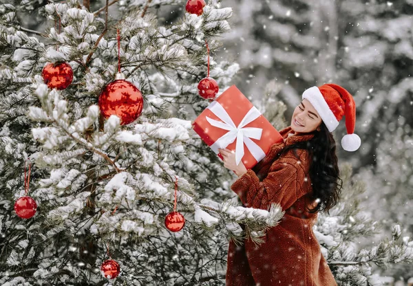 Giovane donna bella sorridente in pelliccia elegante e cappello di Babbo Natale tenere scatola regalo vacanza in mano — Foto Stock