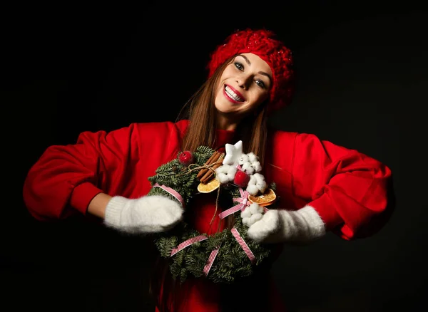 Happy cheerful woman in red winter sweater, warm knitted hat and mittens holds decorated Christmas ornate wreath