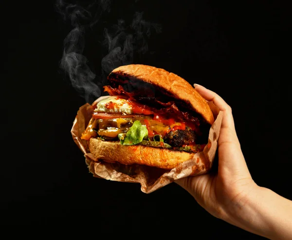 Kobieta ręce trzymać duży cheeseburger grill kanapka z marmuru bekon ser wołowy z dymem parowym — Zdjęcie stockowe
