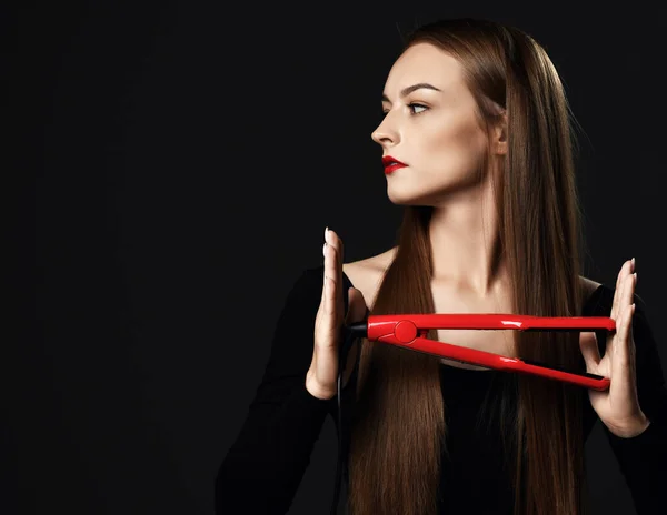 Жінка молода кваліфікована професіонал з шовковистим волоссям тримає червоне волосся випрямляч в руці виглядає осторонь на копіювальному просторі — стокове фото