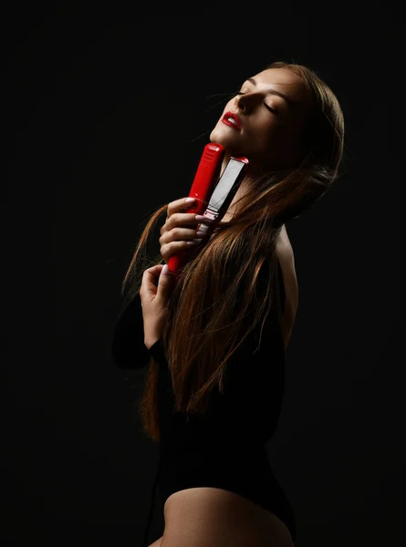 Sağlıklı, ipek gibi uzun saçları olan, gözleri kapalı şehvetli bir kadın yüzüne sarılıyor, kızıl saç düzleştiricisine sarılıyor. — Stok fotoğraf