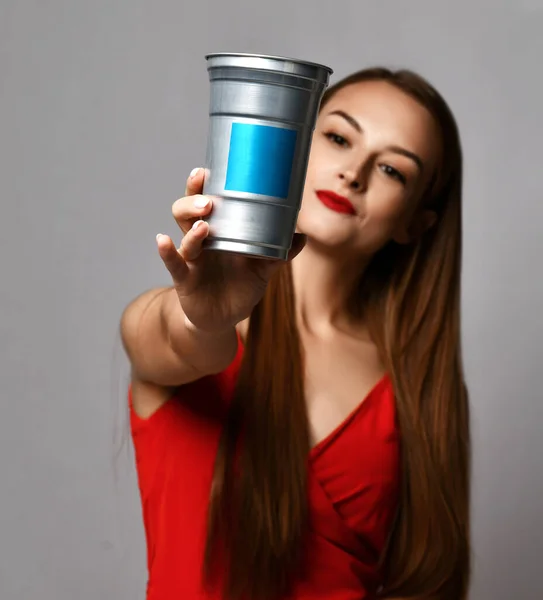 Young woman with long silky straight hair in red dress holding out container with haircare treatment cosmetics
