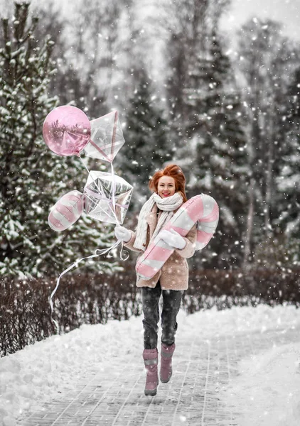 Dziewczyna spaceruje na zewnątrz pod śniegiem z różowymi balonami w pobliżu lasu zimowego. Szczęśliwa ruda kobieta świętuje — Zdjęcie stockowe