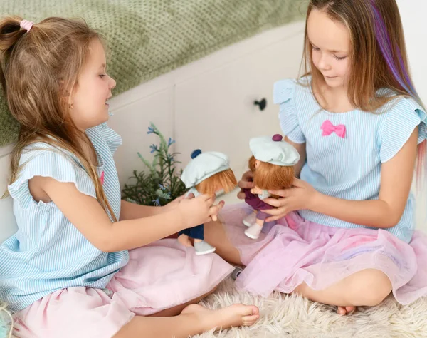 Mavi elbiseli küçük kız kardeşler bebekleriyle birlikte oynuyorlar evdeki yumuşak halıda toplanıyorlar. — Stok fotoğraf