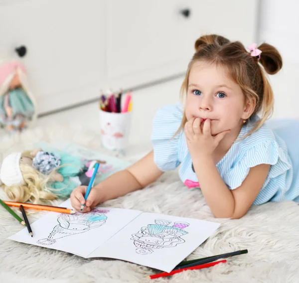 Sakin rüya gören kız yumuşak halıya uzanmış renkli kalemlerle oyuncak bebeklerin resimlerini çiziyor. — Stok fotoğraf