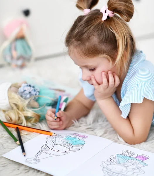 Retrato de menina criança pensativo deitado no tapete macio desenho colorir fotos de bonecas com lápis coloridos — Fotografia de Stock