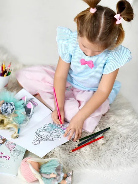 Sakin kız evdeki yumuşak halıya oturup renkli kalemlerle bebeklerin resimlerini çiziyor. Üst görünüm — Stok fotoğraf