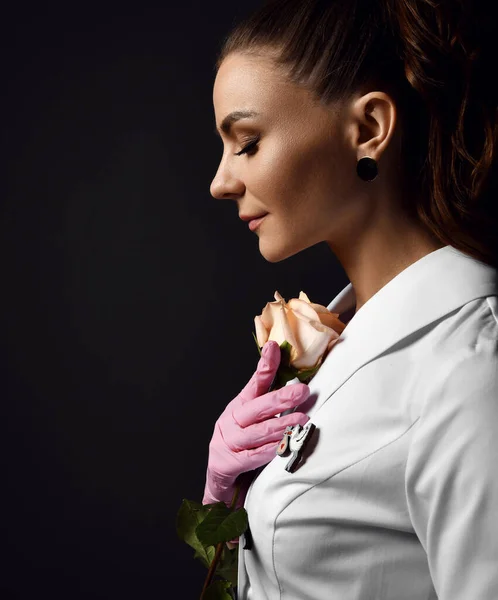 Profile of young pretty woman doctor gynecologist reproductologist in pink latex gloves and uniform standing and holding rose — Stock Photo, Image