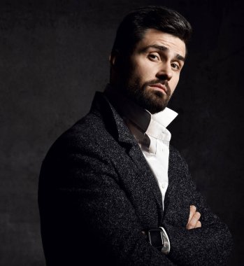 Şık tüvit ceketli genç sakallı adam kollarını kavuşturup bize inançsızlıkla bakıyor.