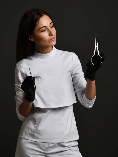 Jeune femme souriante médecin dentiste en uniforme blanc et gants en latex debout tenant des outils dentaires médicaux — Photo