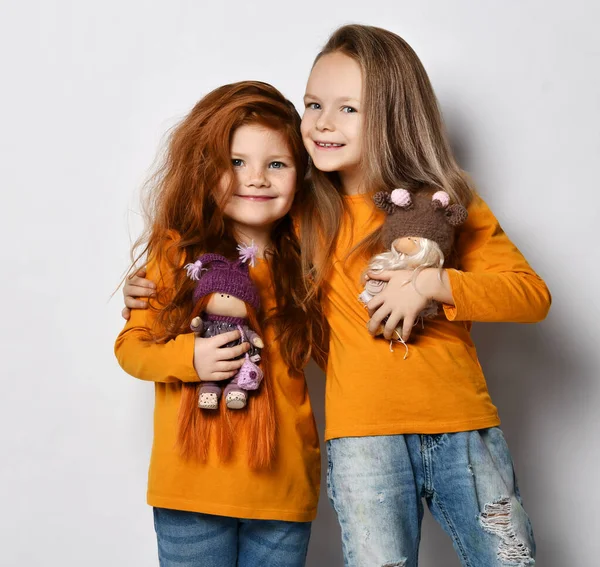 两个穿着相似衣服的快乐女孩的肖像和她们最喜欢的娃娃拥抱着站在一起 — 图库照片