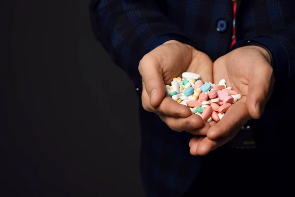 Primer plano de montón de píldoras médicas en las manos del hombre en chaqueta a cuadros sobre fondo oscuro con espacio de copia — Foto de Stock