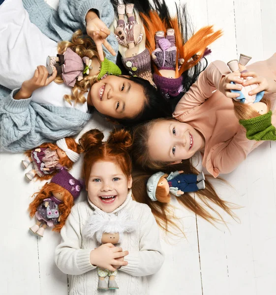 Üç mutlu çocuk, sıcak giysiler içinde ana okulunda oyuncak bebeklerle baş başa yerde yatıyorlar. — Stok fotoğraf
