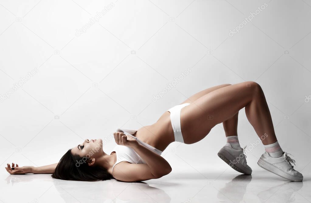 Young sexy brunette woman in white underwear and sneakers lying on floor showing perfect lines of buttocks waist legs