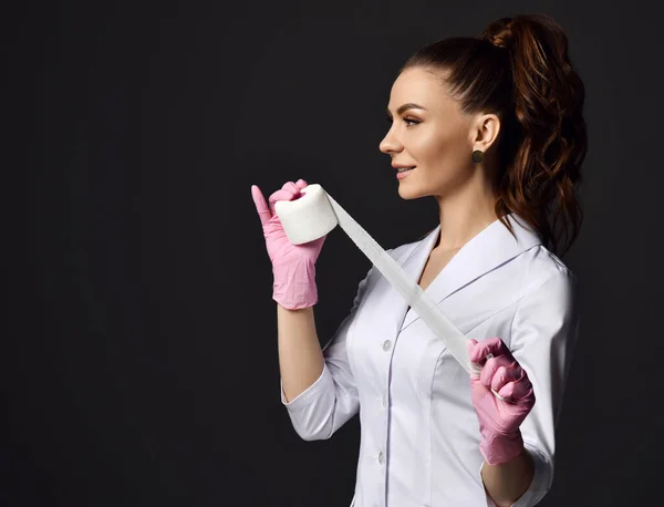 Profil wanita cantik dokter ginekolog atau perawat dalam sarung tangan lateks merah muda dan seragam berdiri memegang perban medis — Stok Foto