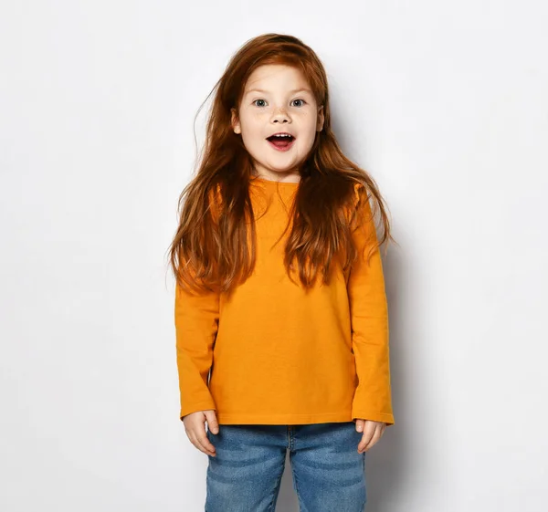 兴奋的红头发小女孩，穿着橙色运动衫和蓝色牛仔裤，张大了嘴 — 图库照片
