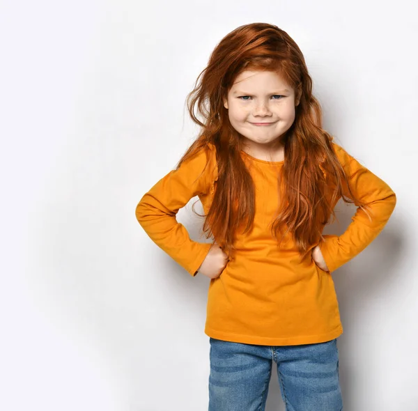 Enfant fille aux cheveux rouges Frolic en sweat-shirt orange et jeans bleus se tient avec des poings à la taille en jouant maman stricte mécontente — Photo