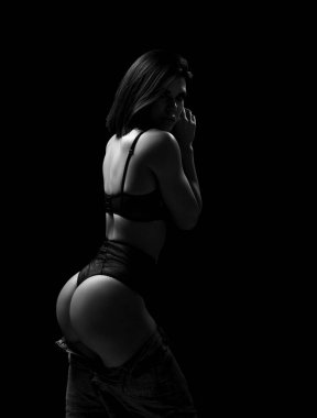 Genç, güzel, seksi esmer kadın model siyah iç çamaşırlarıyla ayakta duruyor ve mükemmel kalçalarını gösteriyor.