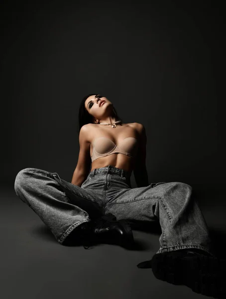 Νέοι αρκετά σέξι μελαχρινή γυναίκα μοντέλο σε τζιν τζιν και σουτιέν κάθεται στο πάτωμα με τα μάτια κλειστά δείχνει τέλειο σώμα — Φωτογραφία Αρχείου