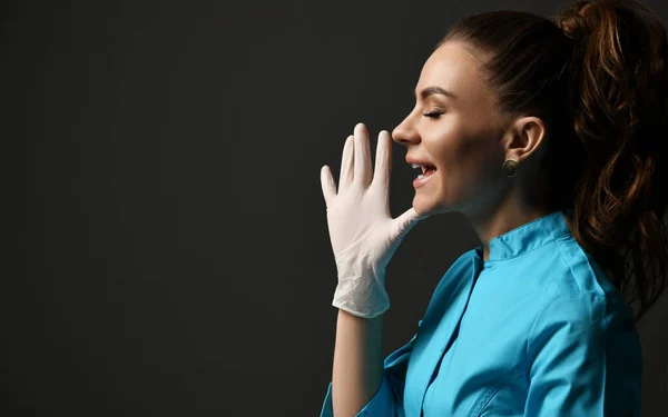 Hablar o gritar joven doctora en bata médica azul y guantes de látex sostiene la mano con los dedos extendidos en la cara —  Fotos de Stock