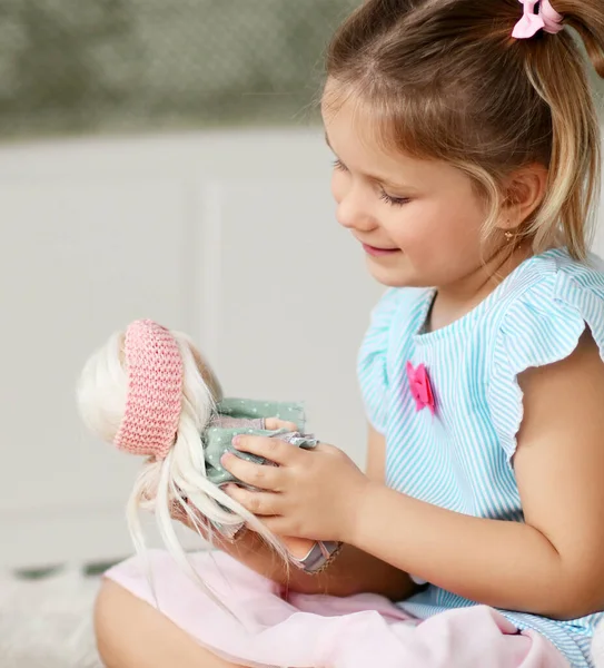 Портрет милой девочки в домашнем платье сидя на мягком ковре дома, играя разговаривая со своей любимой куклой — стоковое фото