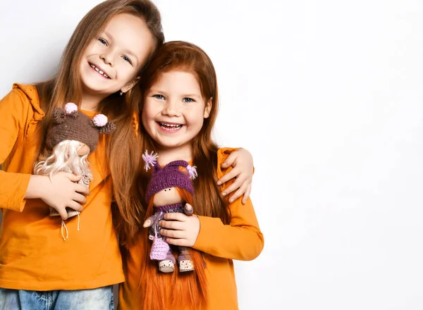 Улыбающиеся маленькие симпатичные девочки-сестры в терракотовых желтых удобных одиноких повязках стоят, обнимая игрушечные игрушки, копируют пространство — стоковое фото