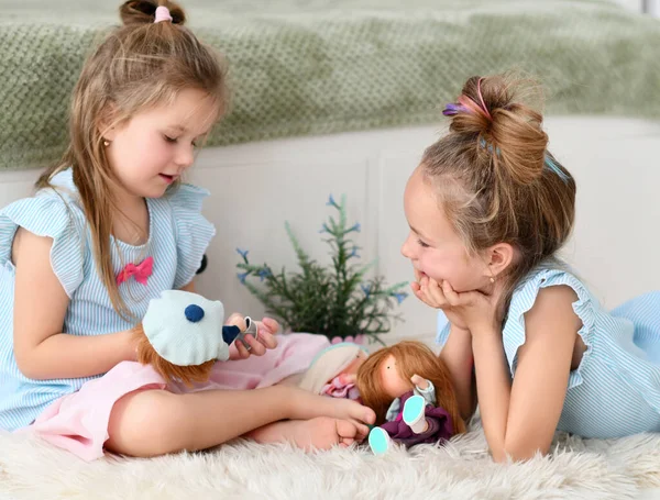 Старшая сестра девочки в домашнем платье слушает рассказы своей младшей сестры. Дома они играют с новыми игрушками. — стоковое фото