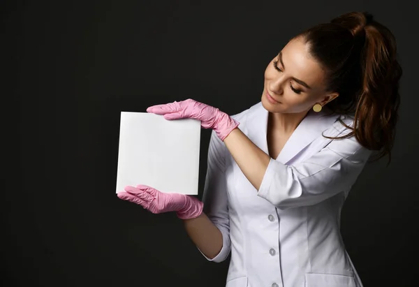 Young smiling pretty woman doctor therapist in white uniform and protective latex gloves holding blank paper sheet — Stok fotoğraf