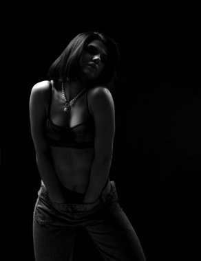 Siyah iç çamaşırlı, mükemmel vücutlu heyecanlı seksi kadın pantolonunun içinde el ele tutuşup kendine dokunuyor. Siyah ve beyaz.