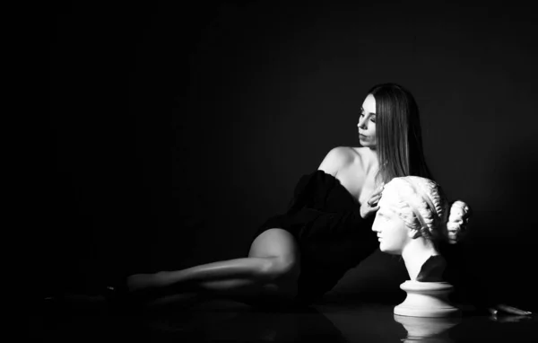 Czarno-biały portret młodej wspaniałej szczupłej seksownej kobiety w czarnej sukience leży na podłodze w profilu rzeźby — Zdjęcie stockowe
