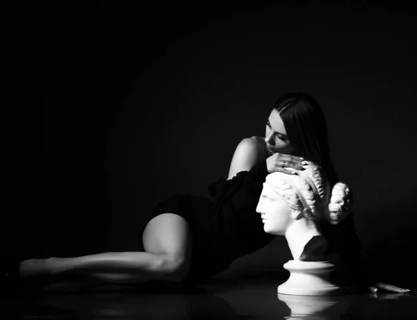 Retrato en blanco y negro de sensual mujer sexy delgada en vestido ajustado negro acostado en el suelo apoyado en el perfil de la escultura —  Fotos de Stock