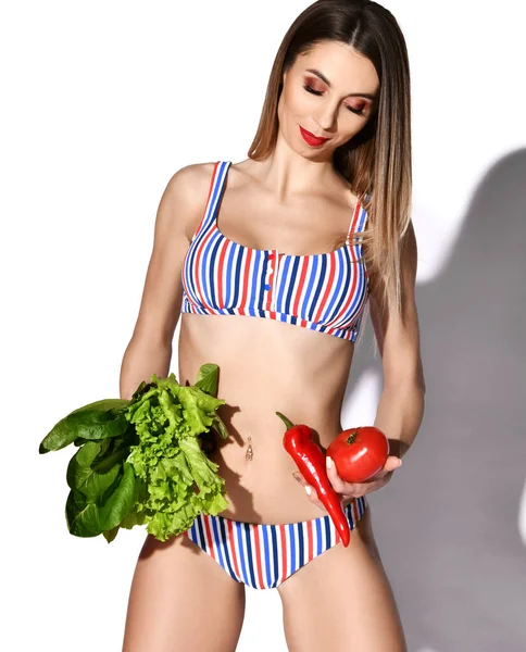 Молодая положительная улыбка стройная красивая сексуальная женщина с идеальной фигурой в полосатых купальниках стоя и держа свежие овощи — стоковое фото