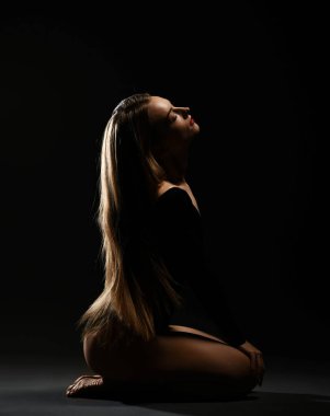 Uzun, ipek düz saçlı, koyu renk elbiseli, ince tenli kadın dizlerinin üzerine çöküp gözleri kapalı oturuyor.