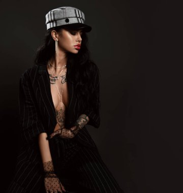 Sarkık dudaklı, kollarında mücevher dövmesi olan çıplak vücutta ince çizgili pantolon giymiş bir kadın portresi.