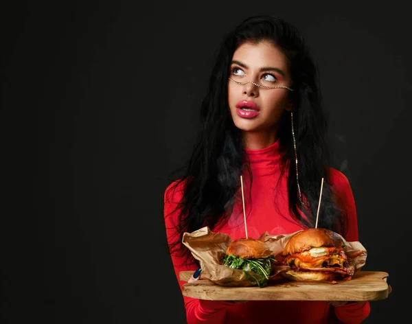 Güzel bir kadın elinde iki ev yapımı hamburger sandviçi ve pembe kırmızı bluzlu sıcak buharlı çizburger ile köşeye bakıyor. — Stok fotoğraf