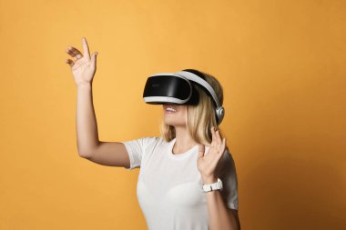 Tişörtlü sarışın kadın VR gözlüklü gelişmiş kullanıcı teknolojisi sanal gerçeklik tuşuna basıyor. Yan görünüm