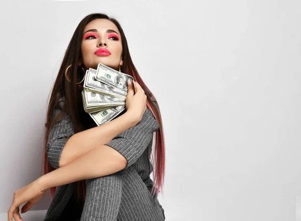 Rijk rijk brunette vrouw in grijs pinstripe broekpak zit op kopieerruimte houden bundel dollars geld in het gezicht — Stockfoto