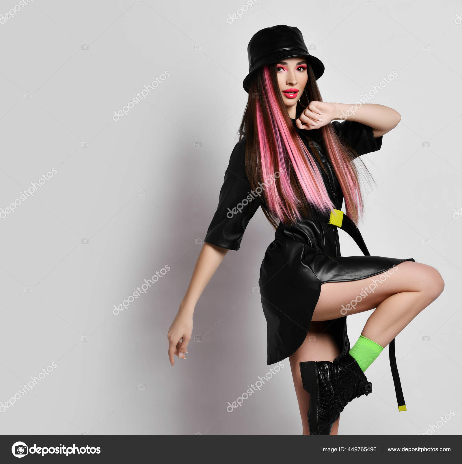 Sexy slim woman with pouty lips in short leather mini dress and hat stands sideways to camera with her knee up marching Stock Photo by ©dml5050 449765496 pic picture