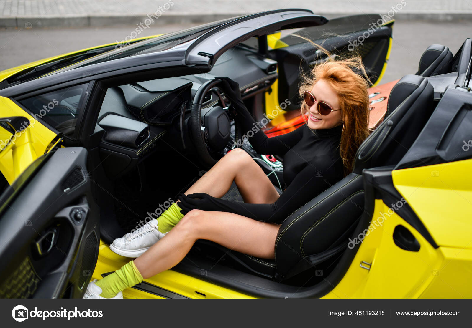 Feliz sorrindo rica mulher ruiva em roupas pretas com pernas nuas e luvas  longas senta-se ao volante do carro esporte — Foto © dml5050 451193218