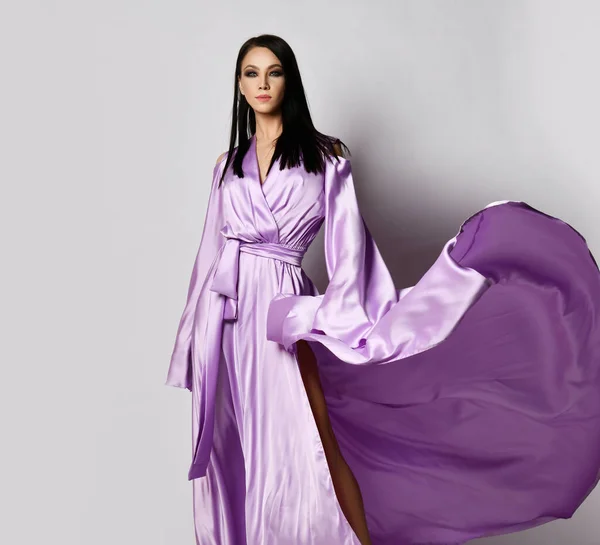 Junge hübsche brünette Frau in lila langen Maxi-Kleid Seidenkleid steht mit dem Saum flattert im Wind — Stockfoto