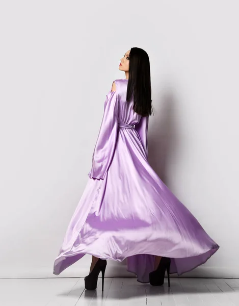 Junge hübsche Frau in lila seidigem fliegendem Maxi-Kleid und Schuhen, die nach der Laser-Haarentfernung leicht und weich nach hinten stehen — Stockfoto